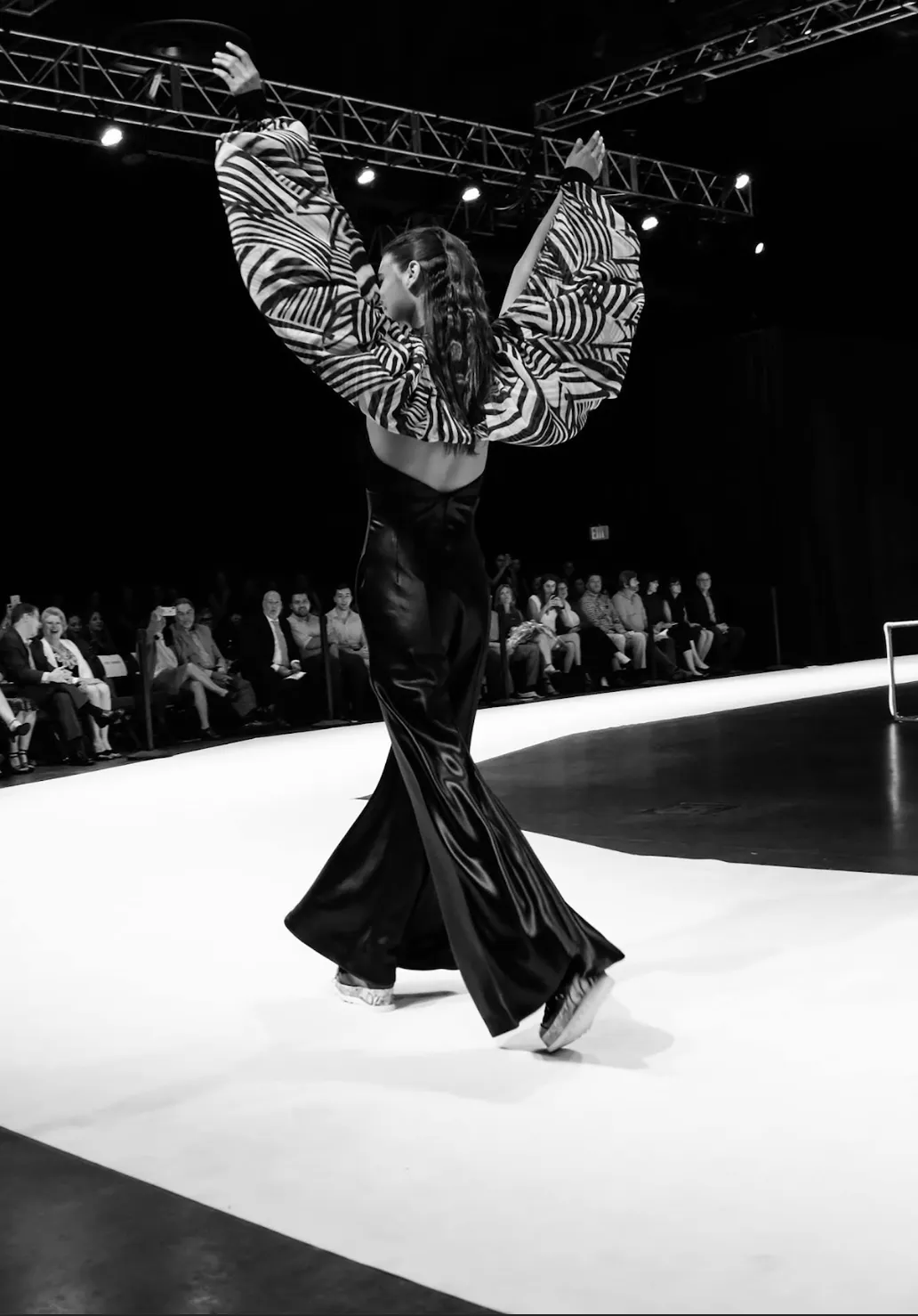 Dramatic black and white runway photo of Marist College Senior Thesis collection featuring a model in a black satin jumpsuit with zebra-print sleeves in a dynamic pose